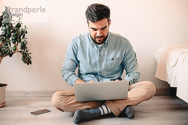 Junger Mann benutzt Laptop-Computer  während er zu Hause auf dem Boden sitzt