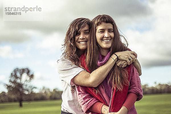 zwei Freundinnen umarmen und lachen im Freien auf grünem Farmland