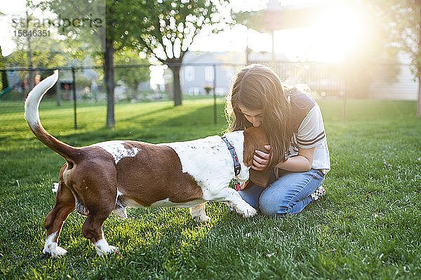 Tweenermädchen küsst Basset Hound Hund auf den Kopf im grünen Gras zu Hause
