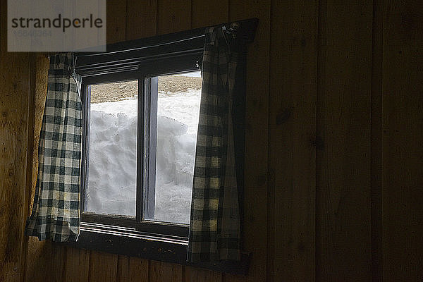 Schnee gegen ein Holzhüttenfenster von innen gesehen
