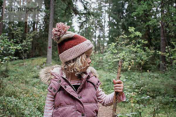 Ein junges Mädchen stand in einem Wald und schaute auf ihren Gehstock und dachte