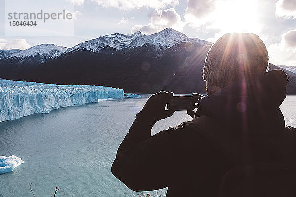 Männlicher Reisender beim Fotografieren mit einem Handy in Gletschernähe an bewölktem Tag