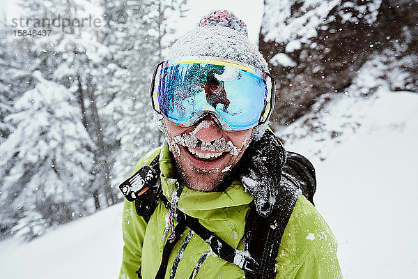 Männlicher Snowboarder im Winter von Schnee bedeckt lächelnd