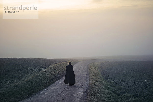 Frau mit langem Mantel geht auf einem Weg im Nebel
