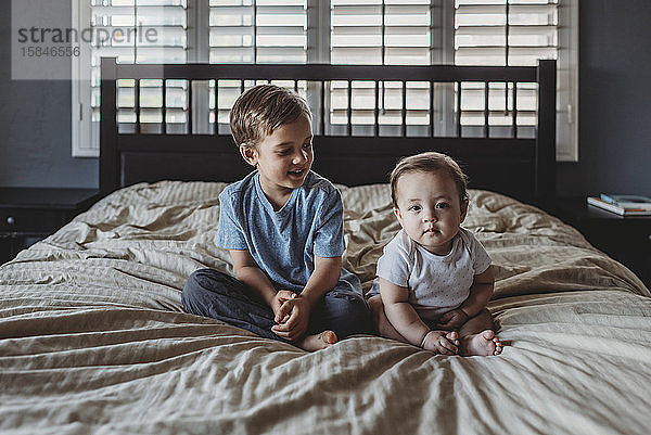 Lächelnder 5 Jahre alter Bruder und kleine Schwester sitzen zusammen auf dem Bett