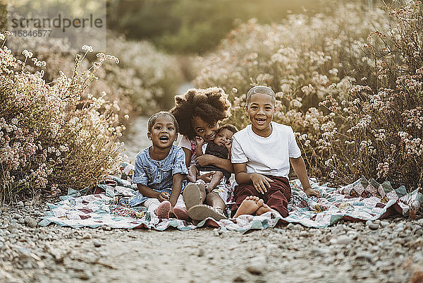 Vier glückliche Geschwister sitzen gemeinsam auf einer Decke im Blumenfeld