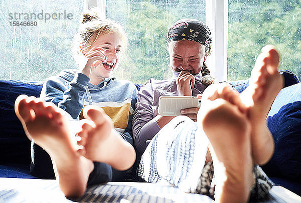 Teenager-Mädchen  die auf einer Couch lachen und etwas auf einem Telefon anschauen