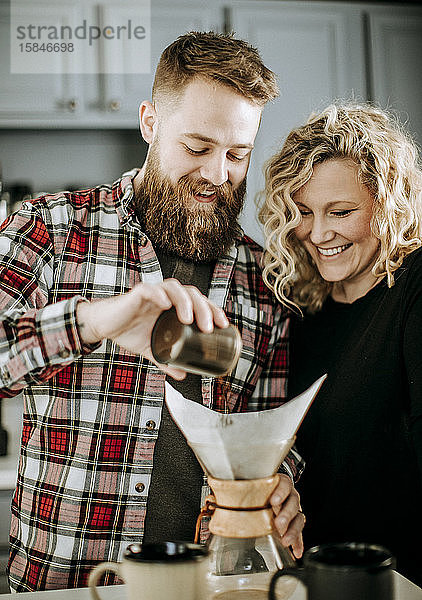 Mann und Frau lächeln  während sie sich darauf vorbereiten  einen Kaffee übergießen zu lassen
