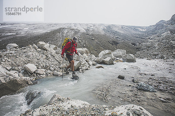 Backpacker überquert Bach unterhalb des schmelzenden Gletschers.