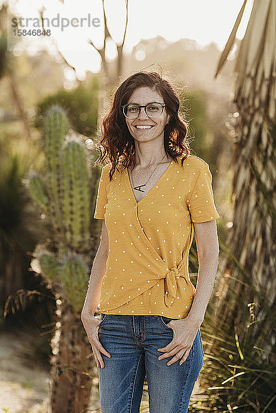 Kopfschuss einer jungen Mutter mit Brille im Gegenlicht eines Kaktusgartens