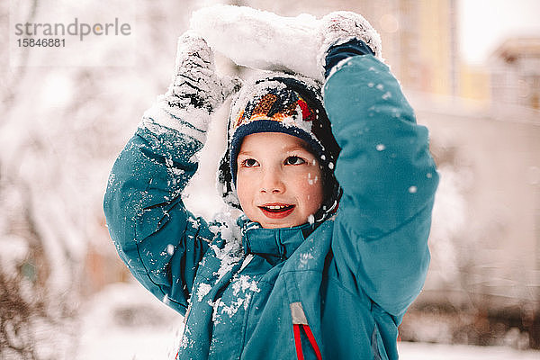 Verspielter Junge  der im Winter einen Schneebrocken über seinem Kopf hält