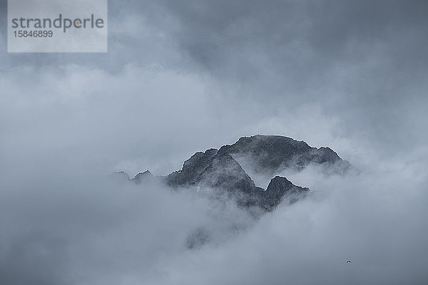 Ferne Bergspitze taucht aus dicken Wolken auf  Reine  MoskenesÃ¸y  Lofoten Inseln  Norwegen