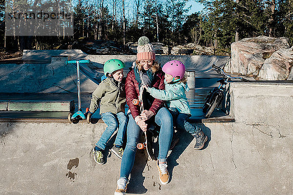 Mutter  die mit ihren Kindern in einem Skatepark mit Fahrrädern und Rollern spielt
