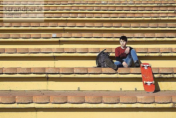 Junger Teenager sitzt auf einer Treppe im Freien und schaut an einem sonnigen Tag weg
