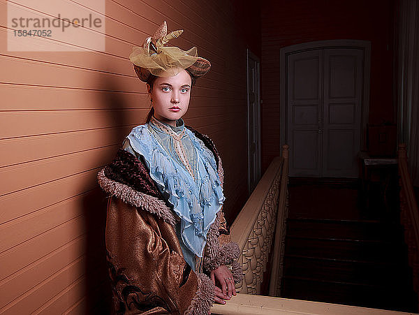 junge Frau in blauem Vintage-Kleid  die in der Nähe der gestreiften Wand steht