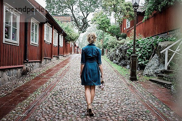 der Rücken einer Frau  die durch eine gepflasterte Straße mit Blumen geht