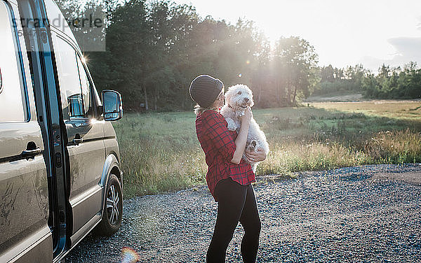 Frau  die im Sommer beim Camping in einem Wohnmobil ihren Hund hält