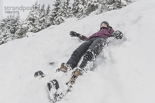 Junge Frau mit Hut rutscht schnell im Schnee bergab lustiges Gesicht