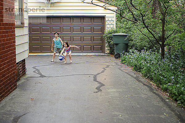 Zwei kleine barfüßige Kinder spielen in der Einfahrt gemeinsam Basketball