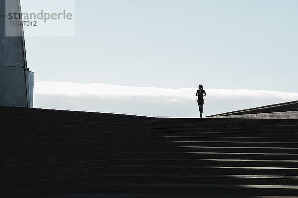 Silhouette einer auf einer Treppe laufenden Frau mit blauem Himmel im Hintergrund