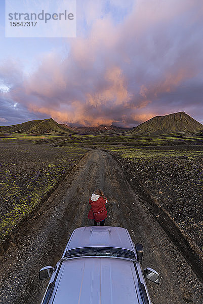 Fotograf beim Fotografieren eines Sonnenuntergangs auf Bergen vor einem Auto