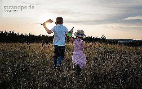 Geschwister laufen bei Sonnenuntergang gemeinsam über eine Wiese und spielen