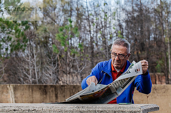 Älterer Mann mit Brille beim Zeitungslesen im Park  Vorderansicht
