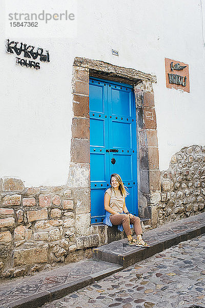 Eine junge Frau sitzt neben einer blauen alten Tür in Cusco  Peru