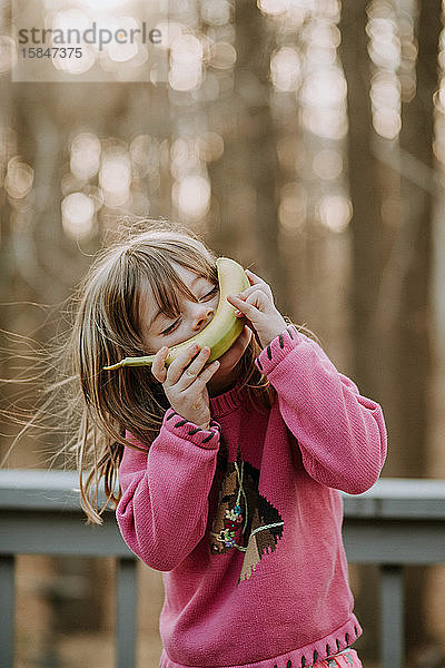 junges Mädchen mit Banane im Gesicht  das draussen lächelt