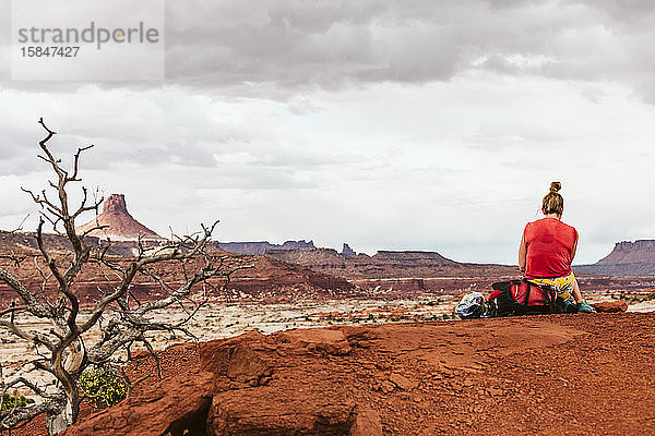 Rucksacktouristin sitzt auf ihrem Rucksack  während sie in der Wüste von Utah eine Pause macht