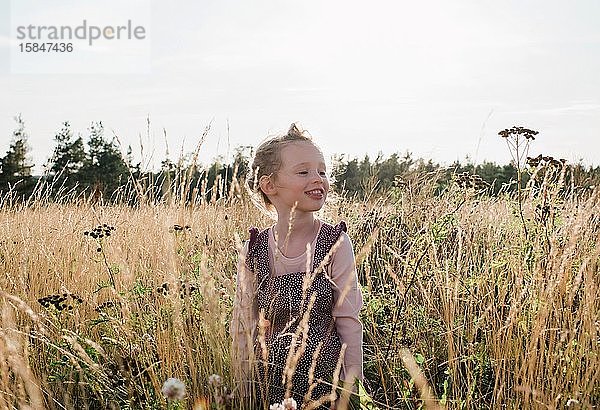 Porträt eines jungen Mädchens  das lächelnd auf einer Wiese mit Wildblumen sitzt