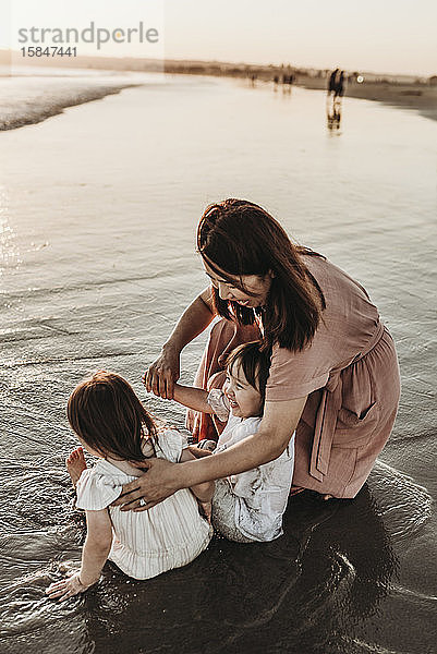 Mutter und kleine Zwillinge spielen bei Sonnenuntergang im Meer