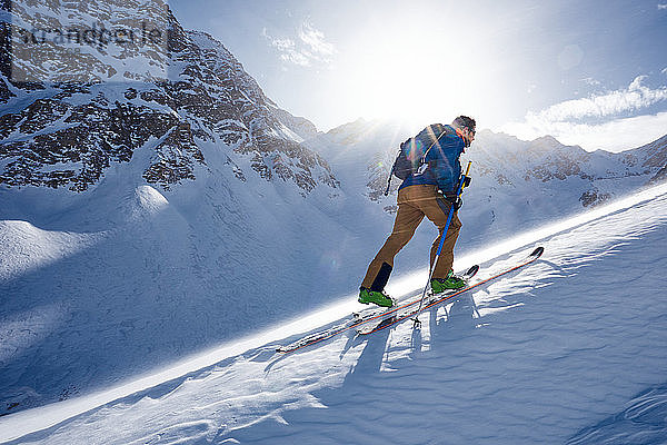 Mann Skitouren bergauf im Wind und im Gegenlicht der Sonne