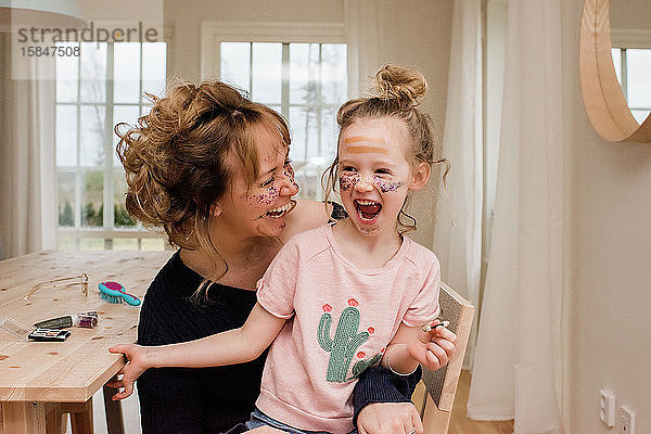 Mutter und Tochter lachen  während sie zu Hause mit Make-up spielen