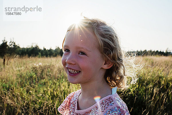 Porträt eines jungen  lockig behaarten blonden Mädchens  das bei Sonnenuntergang draußen lächelt