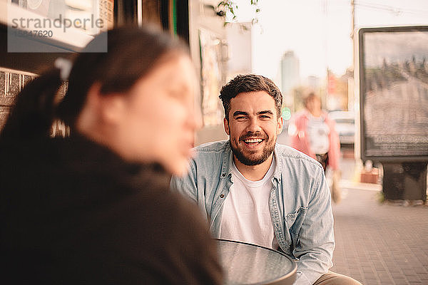 Glücklicher Mann sitzt mit seiner Freundin im Bürgersteig-Café
