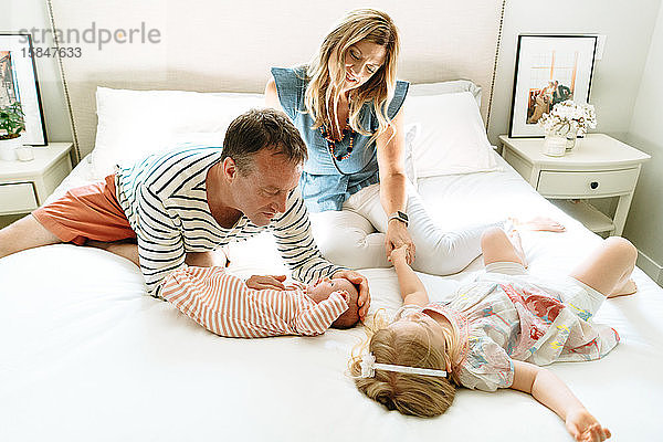 Eine Mutter und ein Vater sitzen zusammen mit ihren Töchtern auf einem Bett