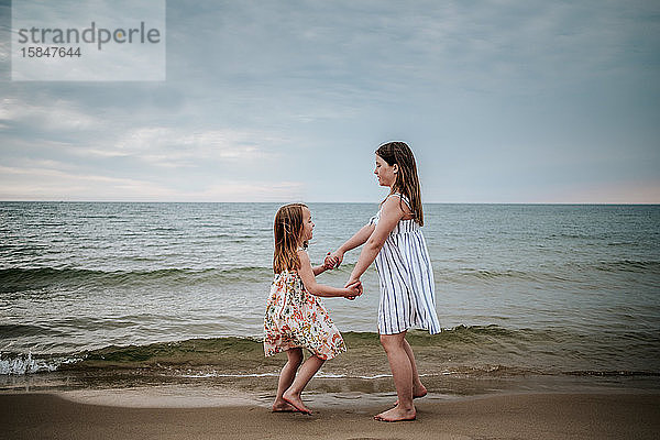 Seitenansicht der Schwestern  die am Strand des Lake Michigan tanzen