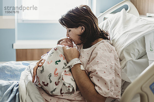 Seitenansicht der Mutter im Krankenhausbett  die den Kopf des neugeborenen Sohnes küsst