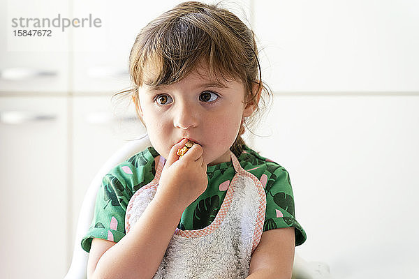 Süßes kleines Mädchen isst Nüsse und sitzt auf einem Hochstuhl