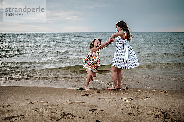ältere Schwester schwingt jüngere Schwester am Strand am Lake Michigan