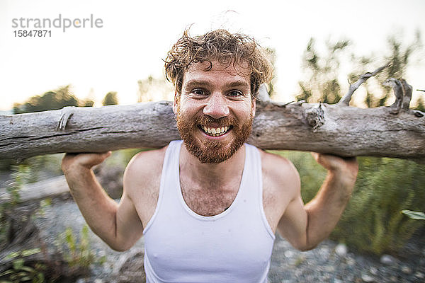 Porträt eines Mannes  der während eines Trainings im Freien Holz auf den Schultern balanciert.