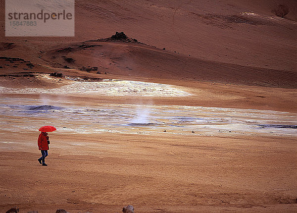 Frau geht mit rotem Regenschirm im geothermischen Thermalquellengebiet Namskard
