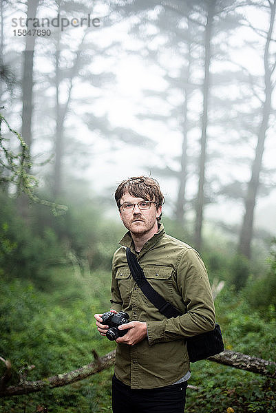Porträt eines Fotografen  der im Freien im Wald steht und eine Kamera hält
