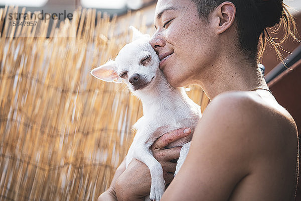 Schöne Frau und winziger Hund lächeln und umarmen sich in der Nachmittagssonne