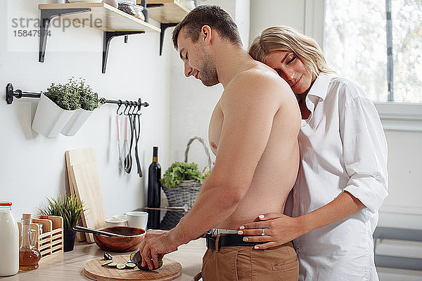 Liebevolles  fröhliches Paar  das sich umarmt und gemeinsam in der Küche kocht