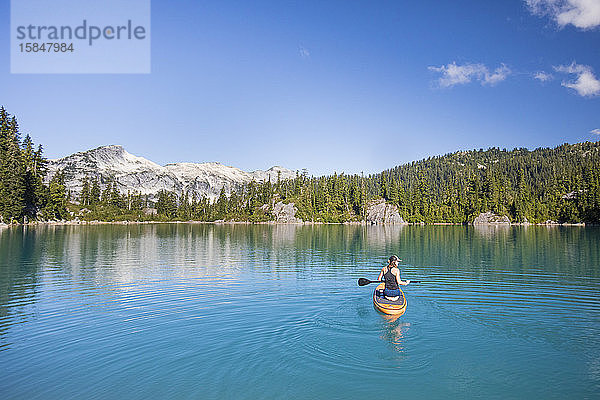 Aktive Frau paddelt stehendes Paddelbrett auf blauem See.
