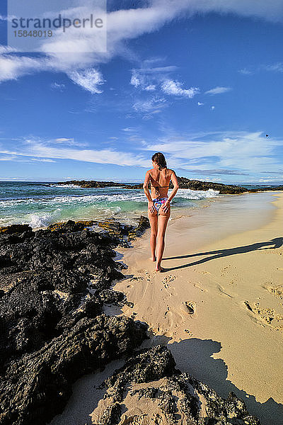 Eine Frau bürstet den Sand von ihrem Bikini  während sie an Makalawena entlang geht
