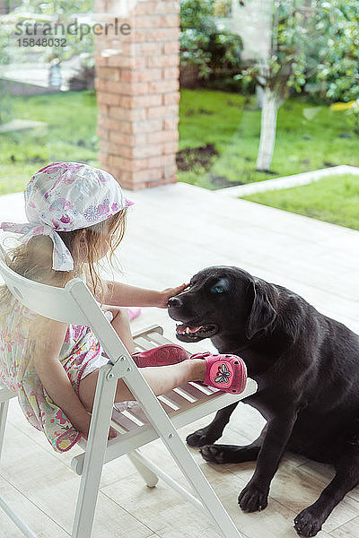 Kleines Mädchen streichelt einen grossen schwarzen Labrador-Retriever-Hund