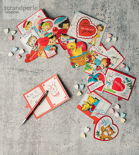 Draufsicht auf Vintage-Valentinskarten und Süßigkeiten auf grauem Hintergrund.